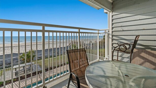 Un balcon avec vue sur la plage, une table et deux chaises.