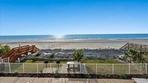 Une vue sur la plage avec une terrasse en bois, une petite construction et une clôture blanche.