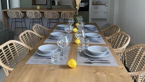 A dining area with a long wooden table set for six, surrounded by wicker chairs.