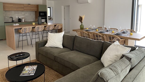 A modern living space with a sofa, a dining table set for four, and a kitchen area.