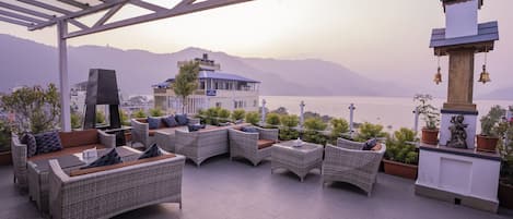 A terrace with wicker furniture, potted plants, and a view of the sea and mountains.