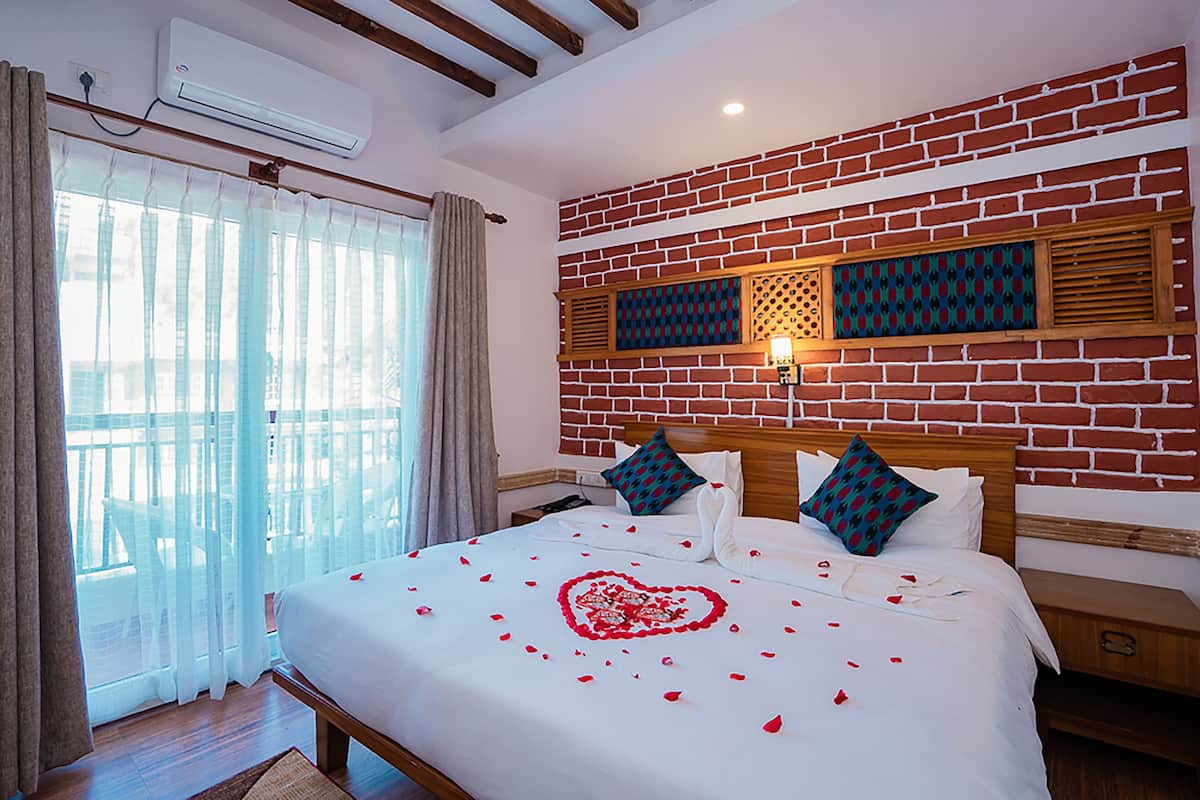 A hotel room with a large bed, a brick wall, and a view through a window with curtains.