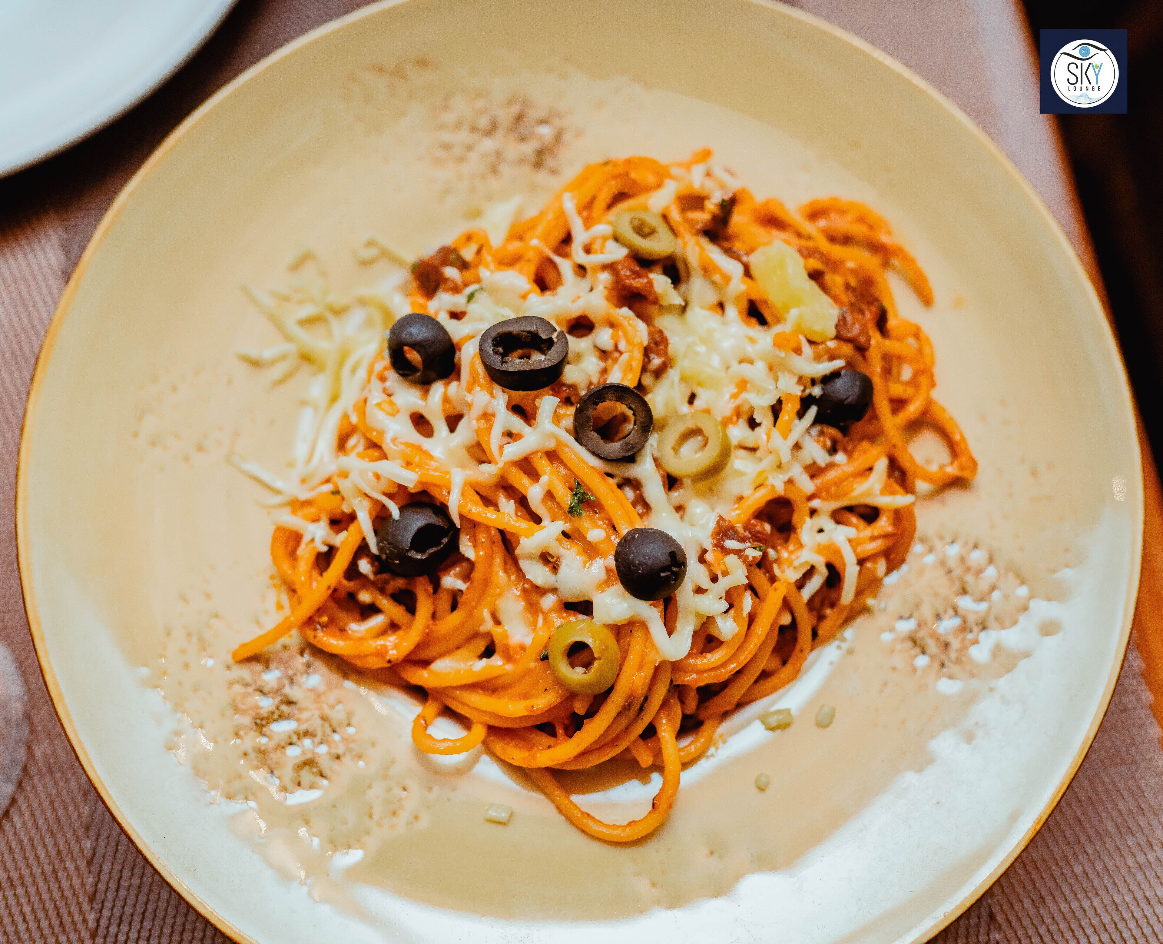 Une assiette de spaghettis avec du fromage et des olives noires.
