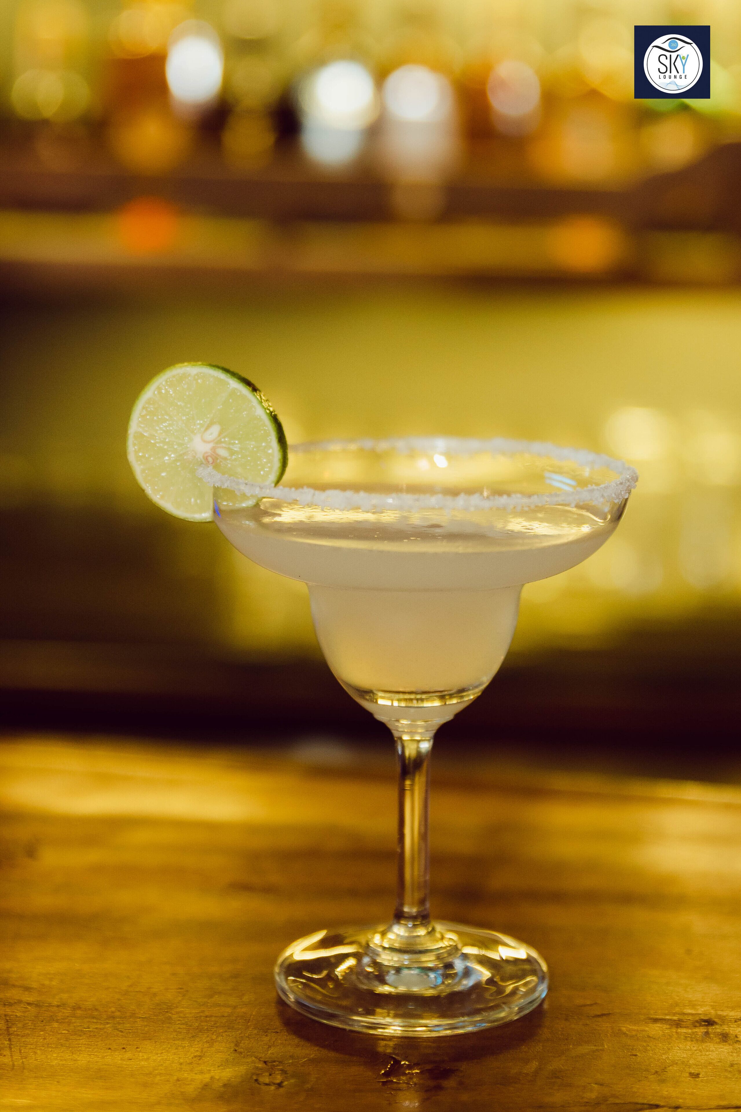 Un verre à margarita, garni d’une tranche de citron vert, posé sur le comptoir en bois d’un bar.