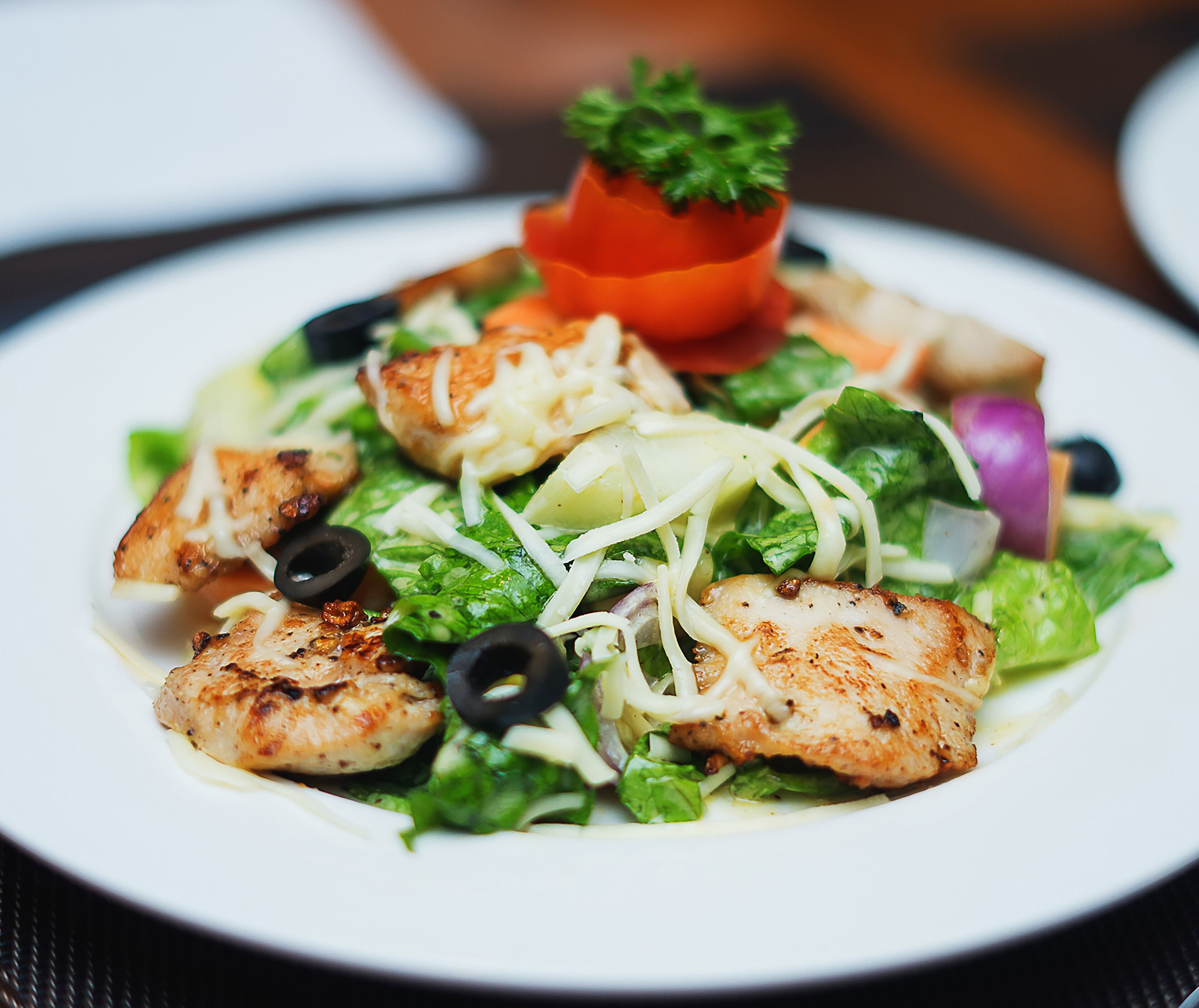 Ensalada de pollo a la parrilla con lechuga, aceitunas negras y un pequeño adorno de tomate.
