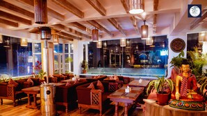 A restaurant with wooden floors, red sofas, and a Buddha statue. - Himalayan Glory Inn (Pokhara)
