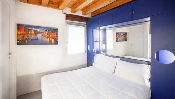 A bedroom with a large bed, a cityscape painting, a mirror, and wooden ceiling beams. - Ca' Gritti (Venice)