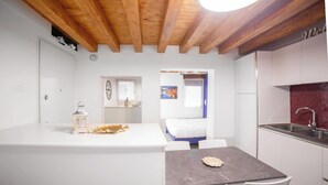 A modern kitchen with white cabinets, a marble countertop, and a wooden ceiling. - Ca' Gritti (Venice)