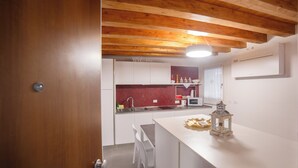A modern kitchen with white cabinets, a red backsplash, and a wooden ceiling. - Ca' Gritti (Venice)
