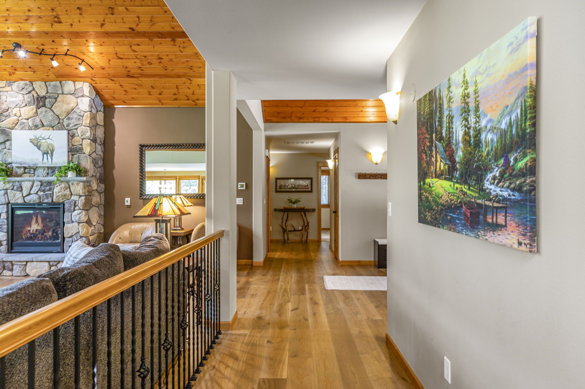 A wooden-floored hallway with a stone fireplace, a sofa, and a painting of a forest scene.