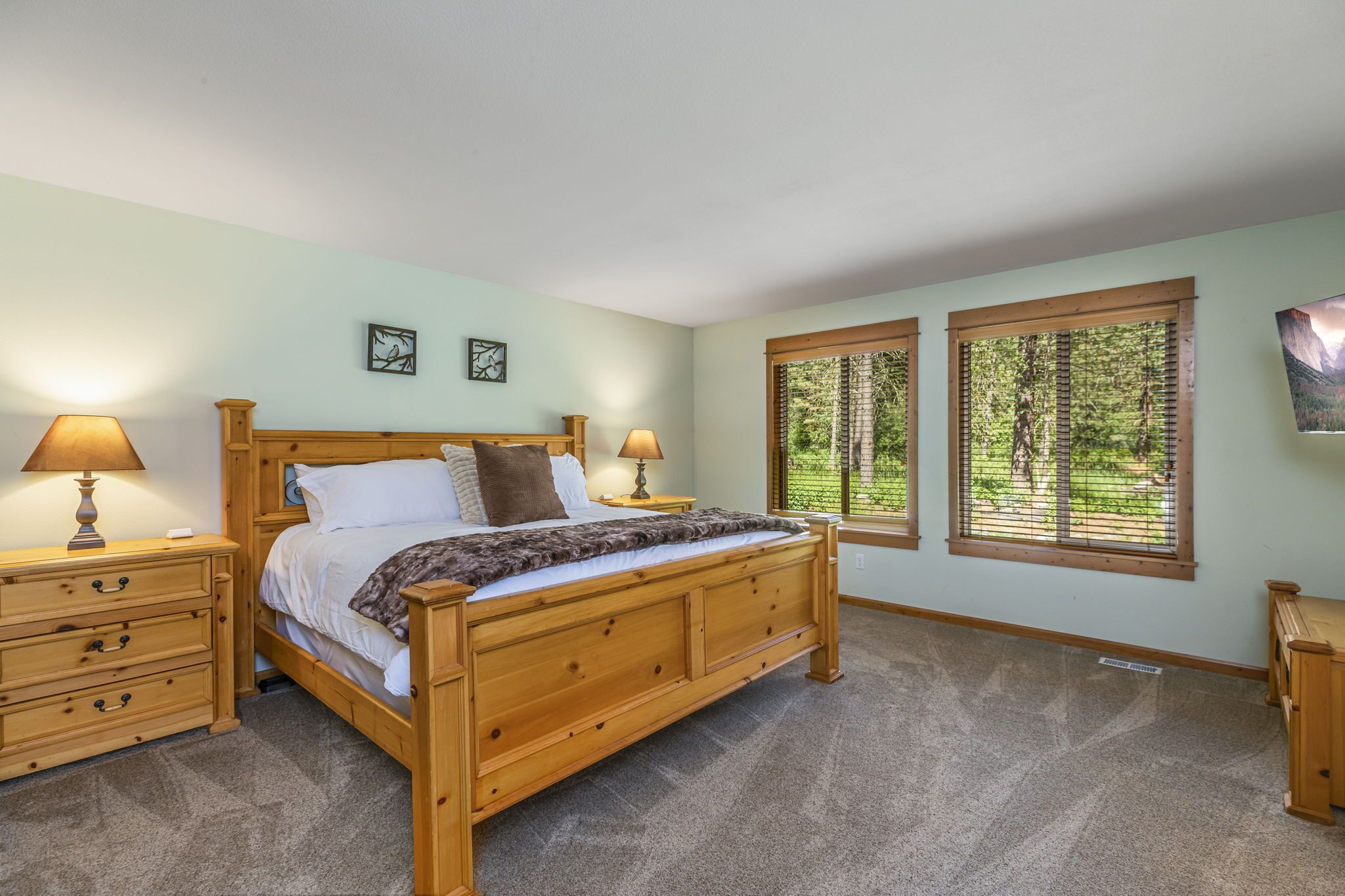 A bedroom with a wooden bed, two bedside tables with lamps, a window with blinds, and a framed picture on the wall.