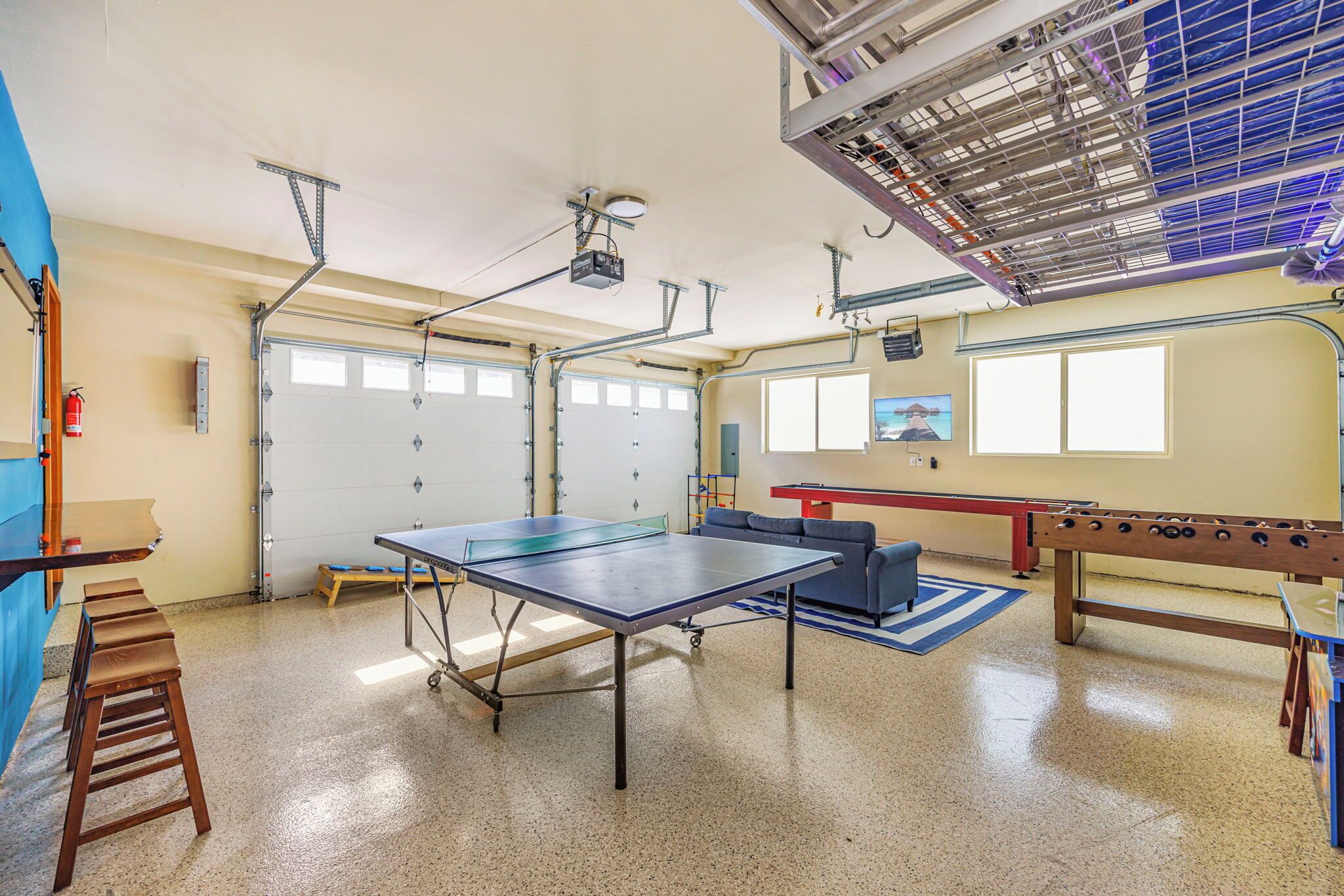 A spacious room with a ping pong table, a foosball table, and a projector mounted on the ceiling.