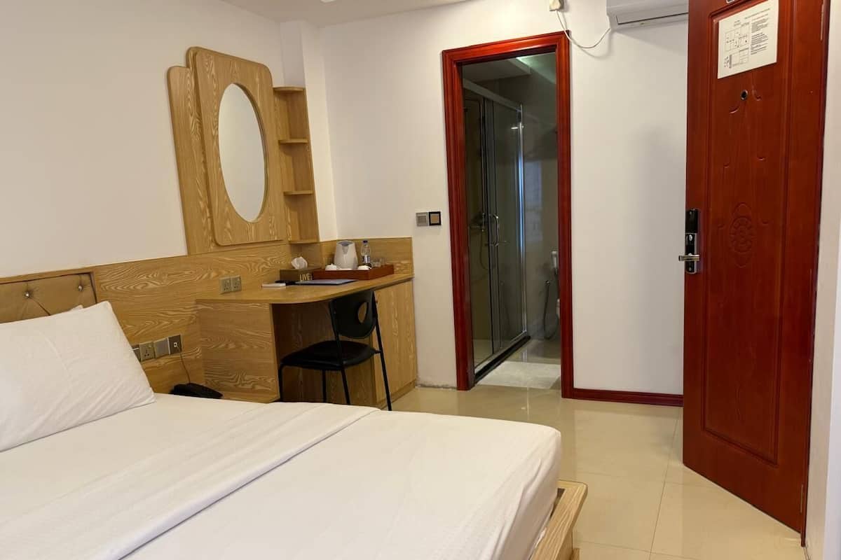 Habitación de hotel con cama, escritorio con silla, espejo y puerta que da a un área de ducha.