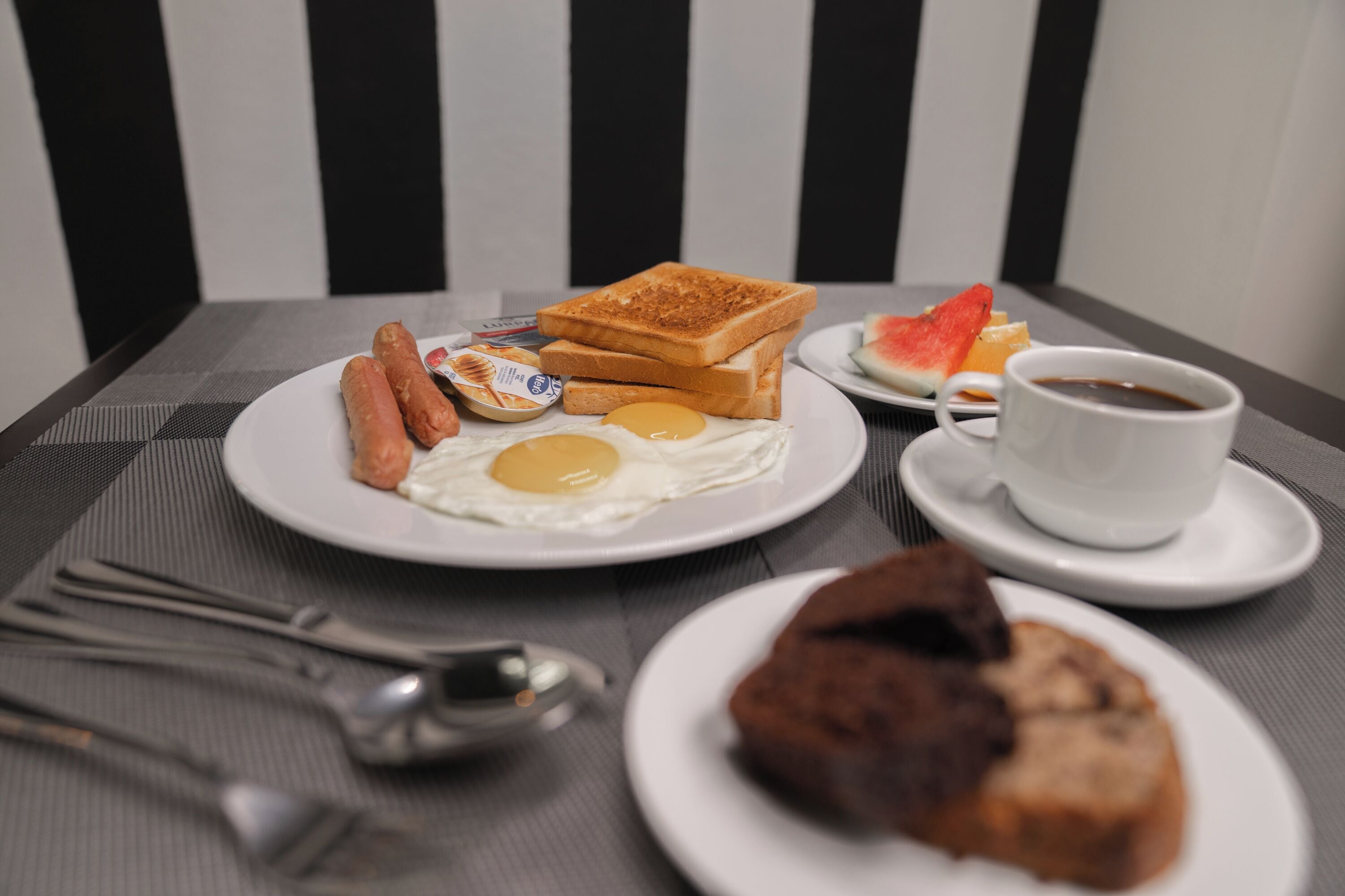 A breakfast plate with toast, eggs, sausages, and a cup of coffee on a table.