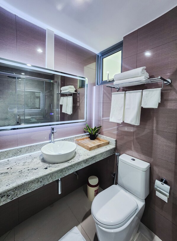 Un baño moderno con encimera de granito, un lavamanos blanco, un espejo y un inodoro.