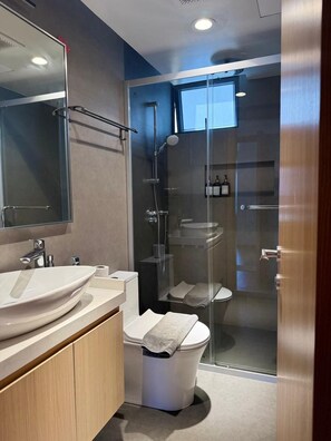 Ein modernes Badezimmer mit einer in Glas abgeschirmten Dusche, einem großen Spiegel und einem Waschtisch mit zwei Becken.