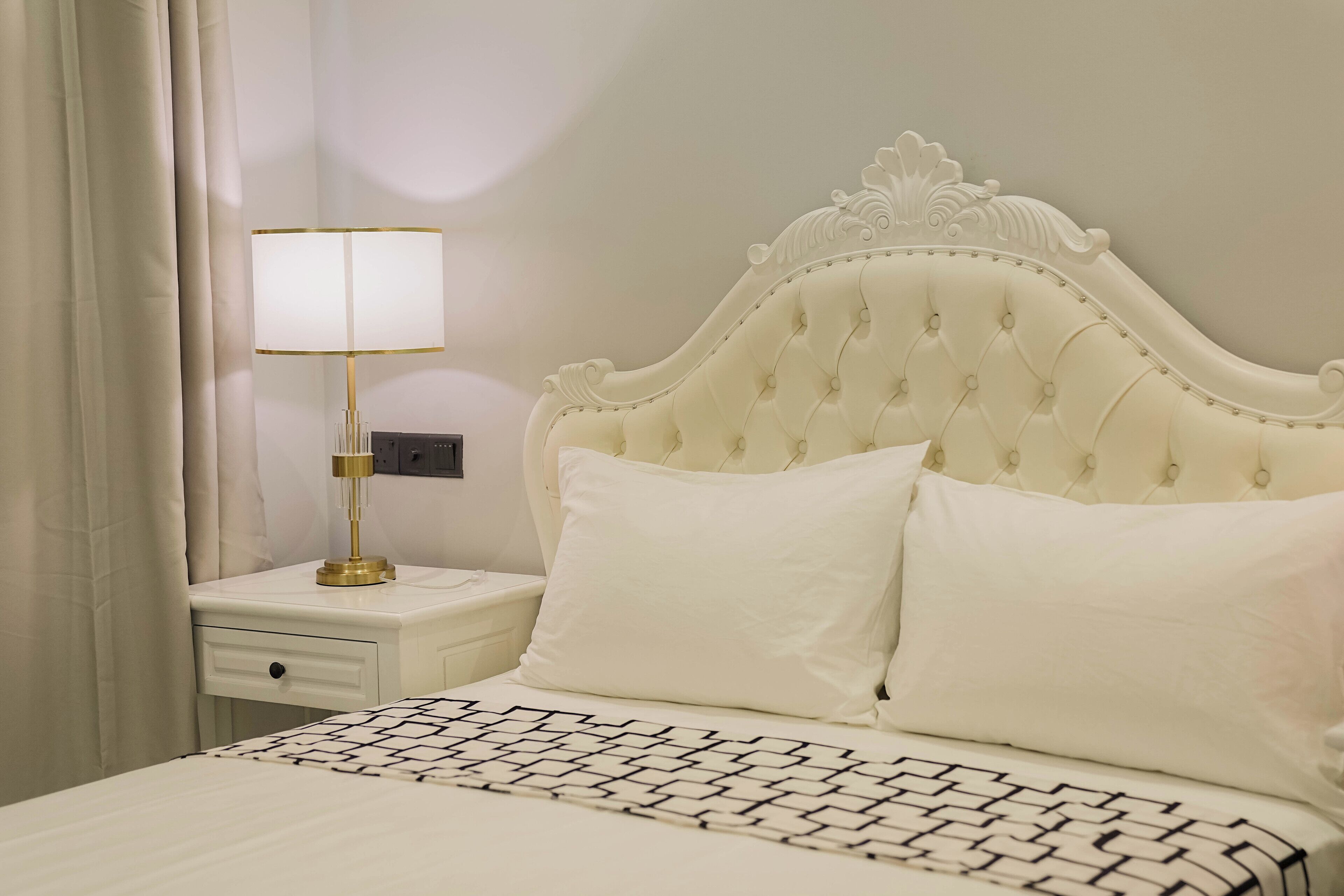 Una cama bien hecha con un edredón estampado, un cabecero blanco y una lámpara de noche.