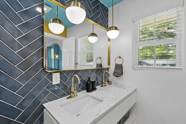 A bathroom with a white sink, gold faucets, a blue and gold mirror, and a window with blinds.