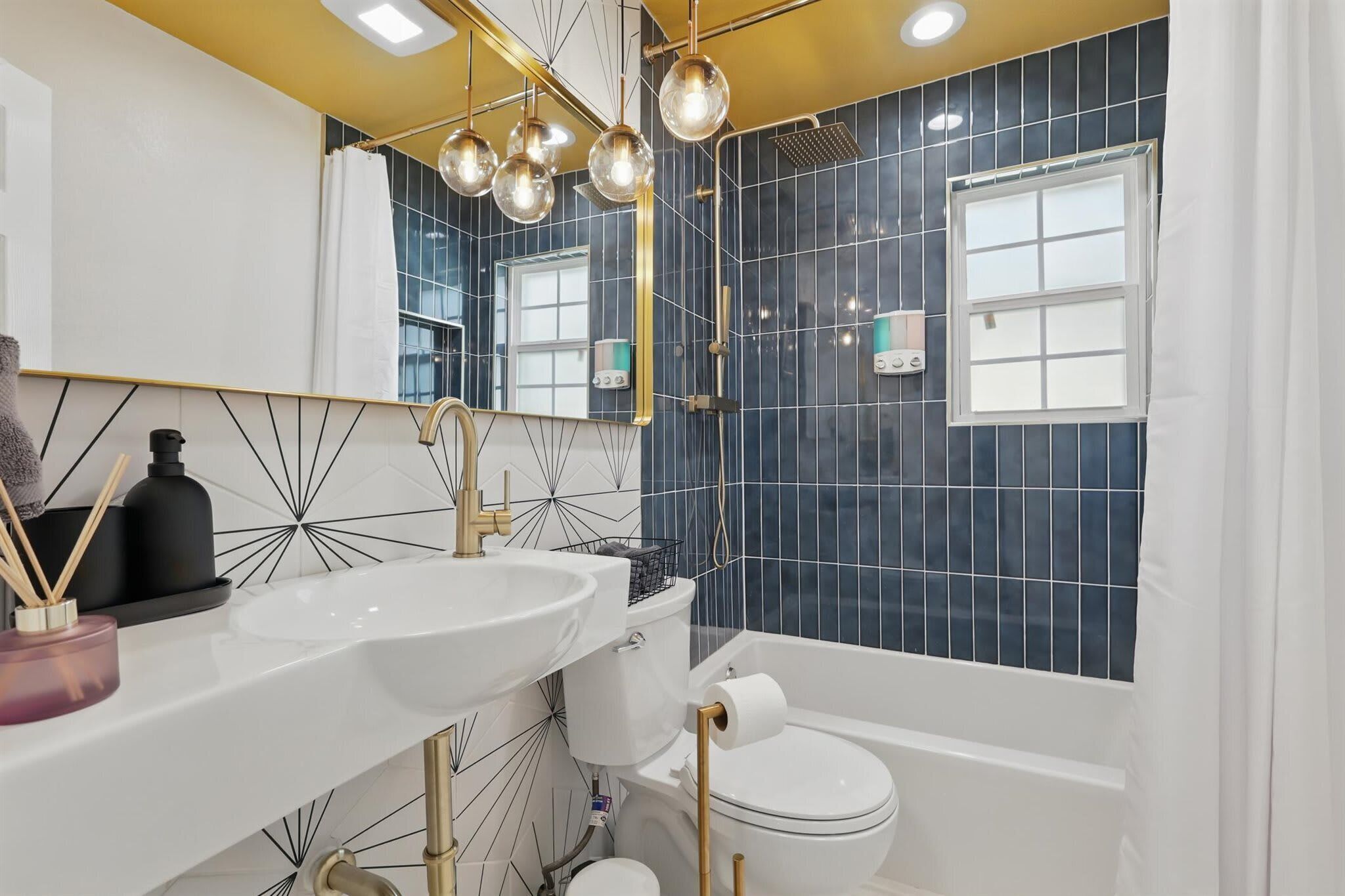 A modern bathroom with a white sink, gold fixtures, and dark blue tiled walls.