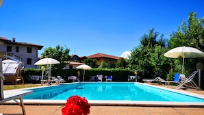 A swimming pool with lounge chairs and umbrellas, surrounded by greenery and buildings. - ALBERGO B&B TENESI (Manerba del Garda)