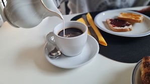 A cup of coffee being poured into a white cup on a saucer, with toast and jam on a plate beside it. - ALBERGO B&B TENESI (Manerba del Garda)