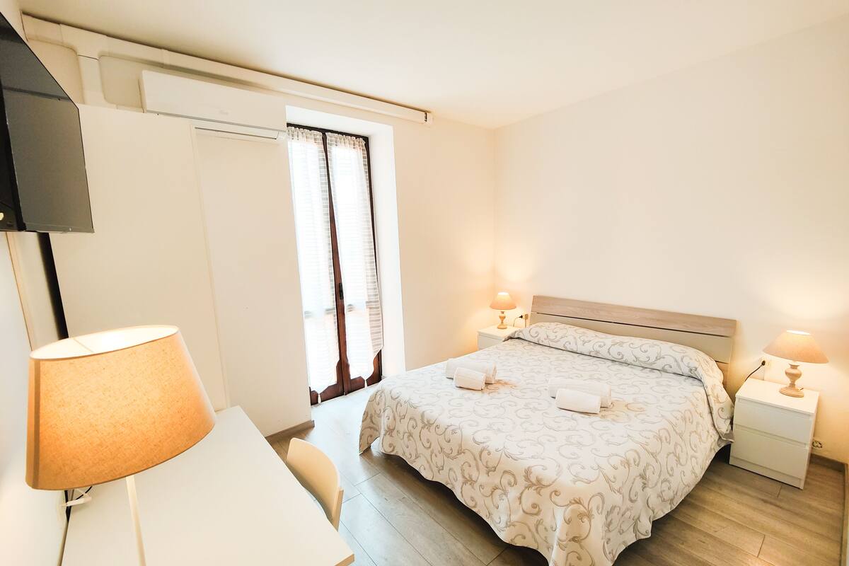 A hotel room with a bed, bedside tables, a desk, and a TV.