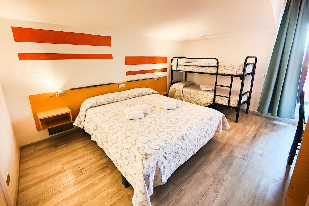 A hotel room with a bunk bed, a single bed, wooden flooring, and a wall with orange accents.