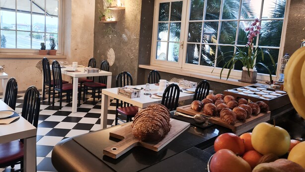 A cafe with checkered flooring, wooden tables, black chairs, a variety of pastries, and a fruit display. - ALBERGO B&B TENESI (Manerba del Garda)