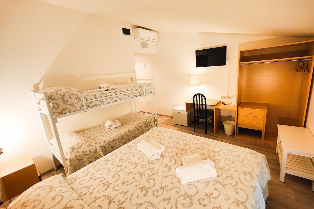 A bunk bed with patterned bedding, a desk with a chair, a TV, and a wardrobe.