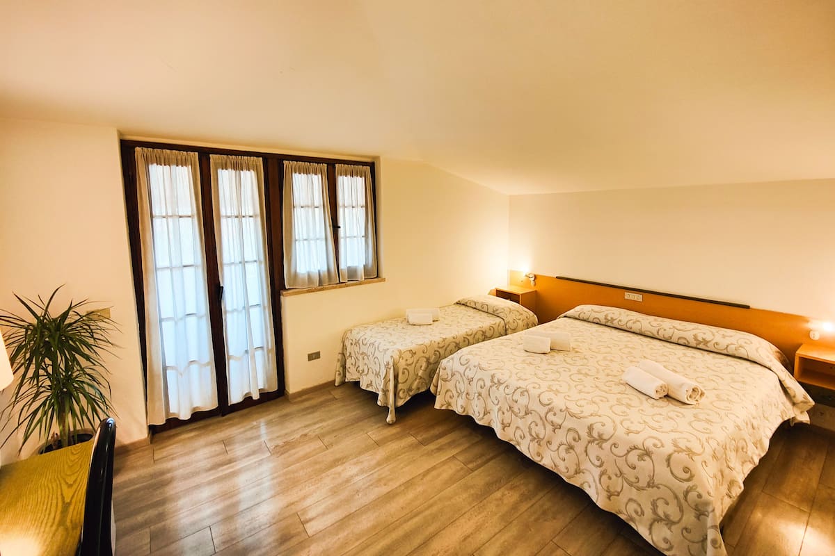 A hotel room with two beds, a wooden floor, a potted plant, and a window with curtains.
