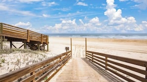 Een houten looppad dat naar een zandstrand leidt, onder een heldere lucht.