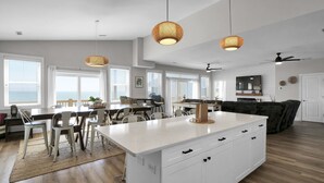 A modern kitchen with a central island, white cabinetry, and a dining area with chairs and a table.