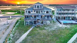 A beachfront property with multiple balconies and a pool, surrounded by a grassy area and a road.