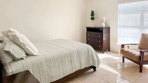 A bedroom with a bed, a dresser, a chair, and a window with blinds.