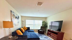 A living room with a sectional sofa, a TV, a lamp, and a painting on the wall.