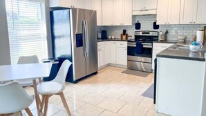 A modern kitchen with white cabinets, stainless steel appliances, and a dining area with white chairs.