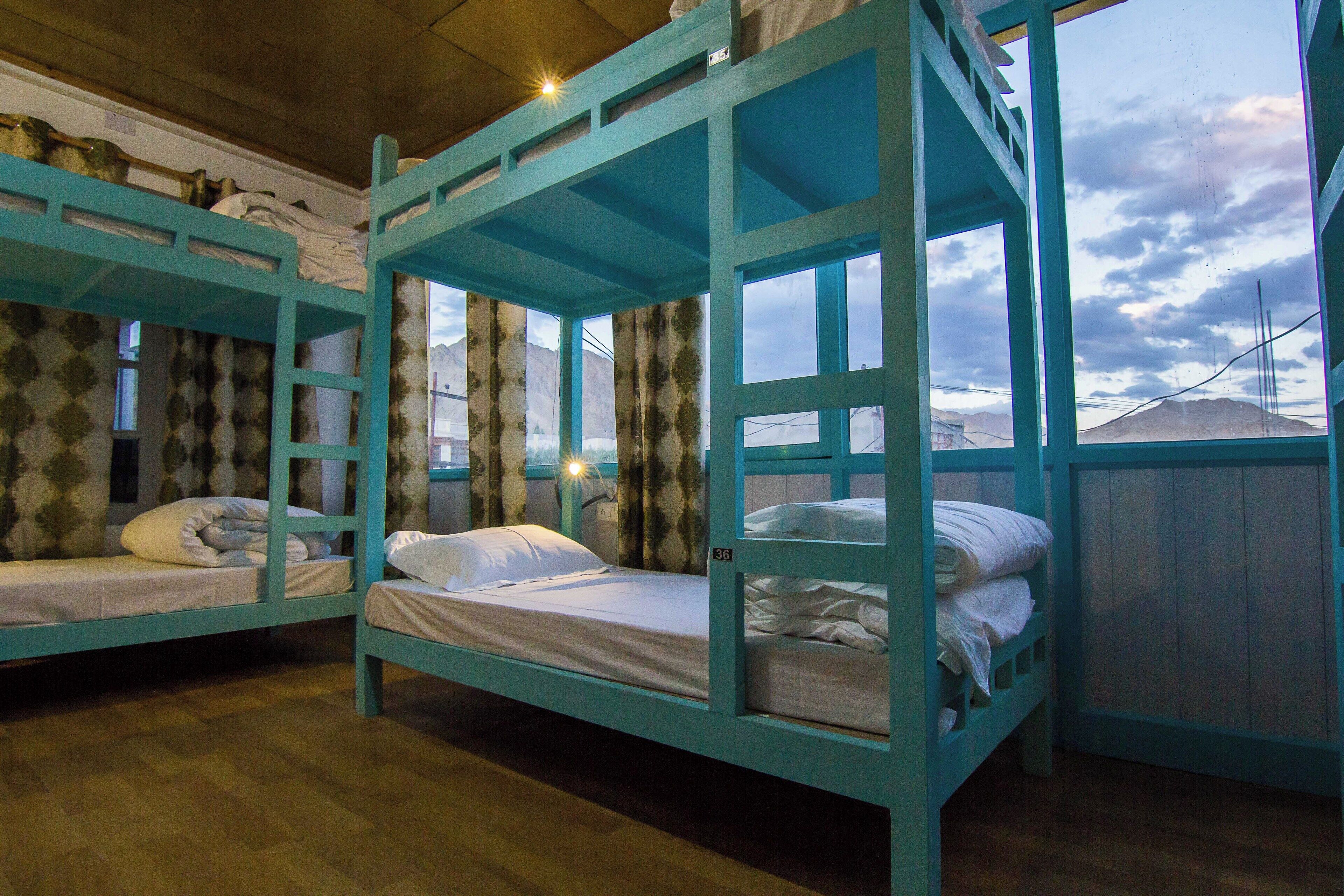 A room with bunk beds, wooden floors, and a window with a view of mountains.