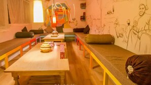A room with a long wooden table, benches, and a sofa. There are wall murals and a hanging light fixture.