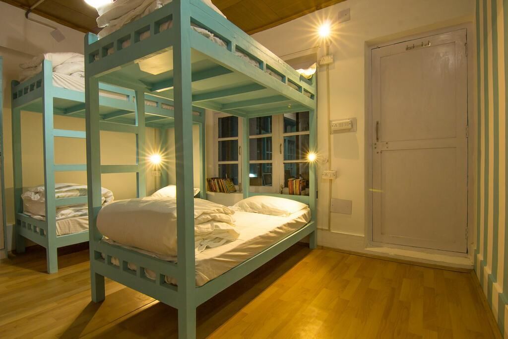 A bunk bed room with a wooden floor, a white door, and a window with curtains.