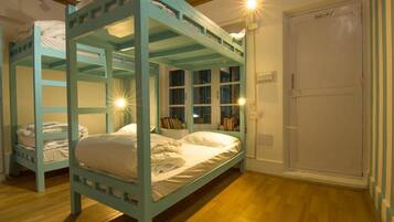 A bunk bed room with a wooden floor, a white door, and a window with curtains.