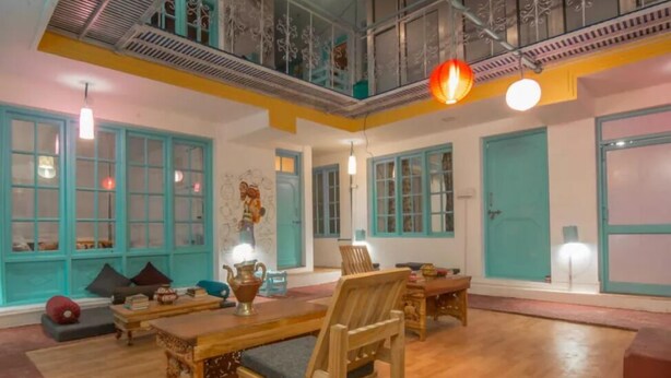 A spacious room with wooden furniture, teal-colored doors, and a high ceiling with exposed beams.