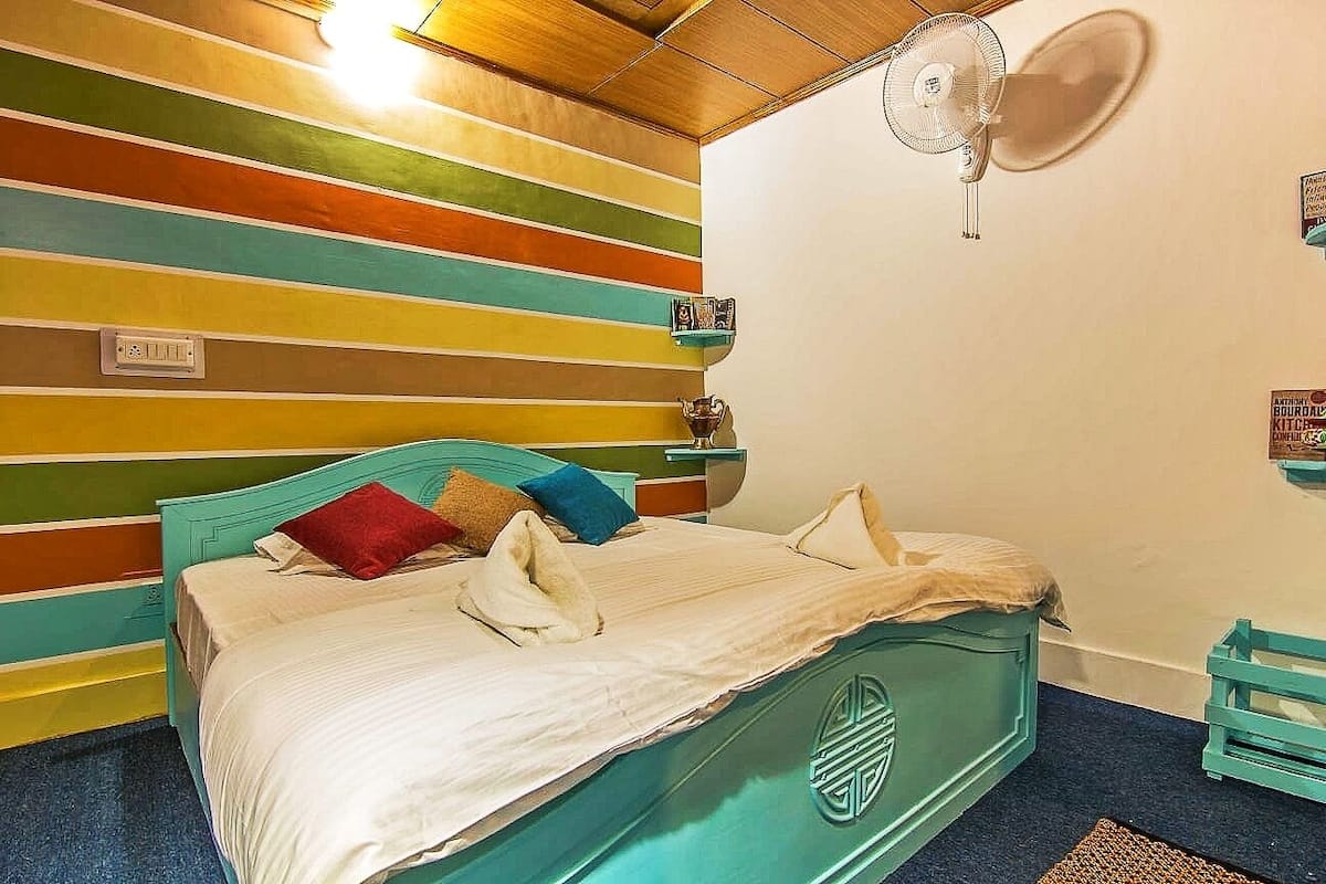 A room with a bed, a fan, and a colorful striped wall.