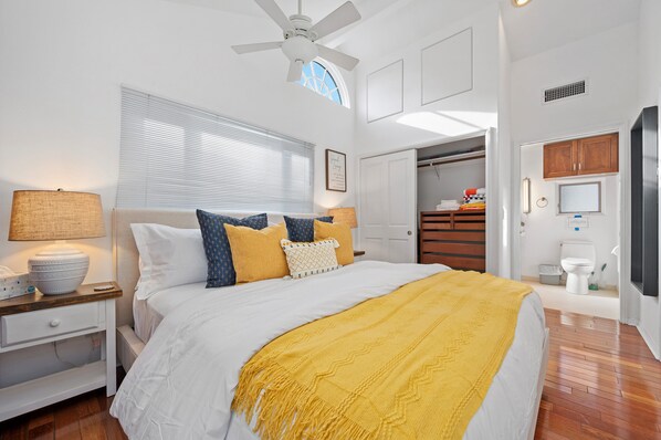 Un dormitorio con cama, mesita de noche, lámpara, ventilador de techo, ventana con persianas, armario y baño con inodoro.