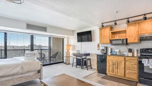 Habitación de hotel compacta con cama, una pequeña mesa de comedor, kitchenette y televisión.