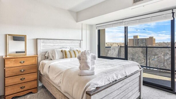 Un dormitorio con un ventanal grande, una cama de madera, un aparador y un espejo.