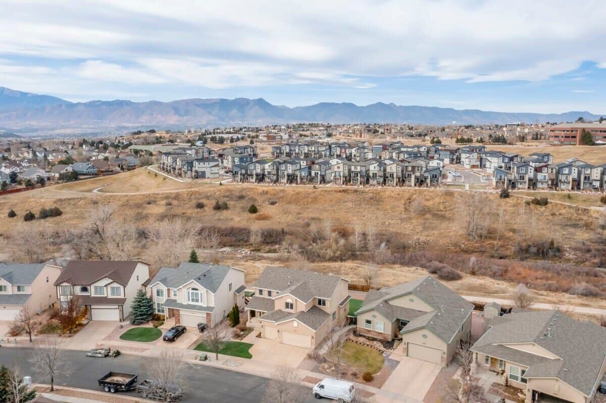 A residential area with multiple two-story houses, a main road, and a mountainous backdrop.