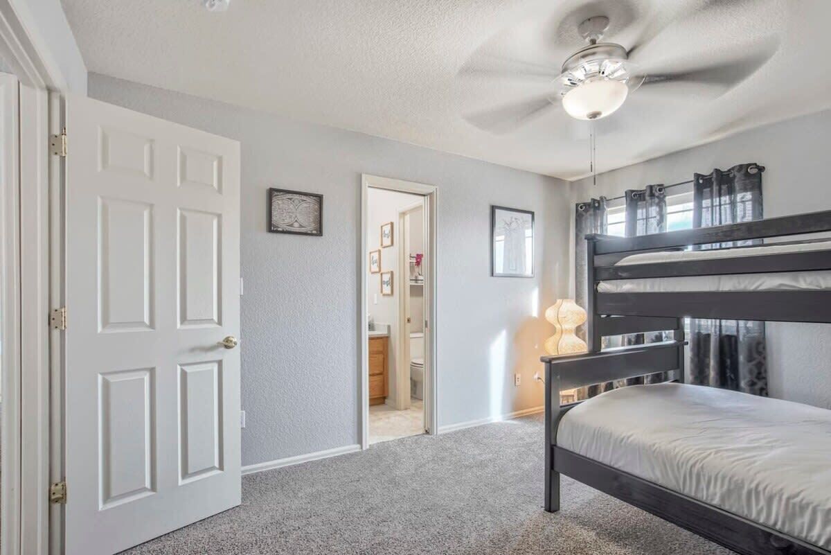 A bedroom with a bunk bed, a ceiling fan, and a door leading to another room.
