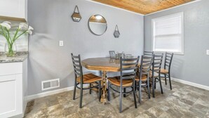 A dining area with a wooden table and chairs, a wall-mounted mirror, and a window with blinds.