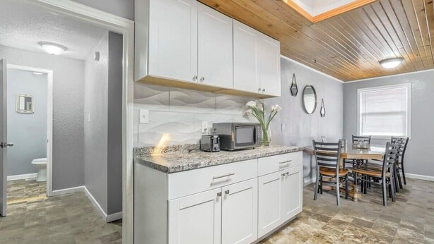 A modern kitchen with white cabinets, a granite countertop, and a dining area with a wooden table and chairs.