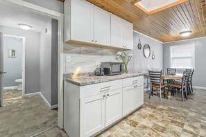 Eine moderne Küche mit weißen Schränken, einer Arbeitsplatte aus Granit und einem Essbereich mit Holztisch und -stühlen.